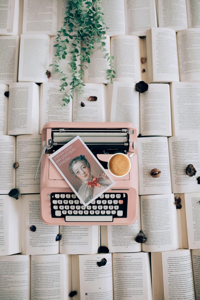 A pink typewriter on open books with a coffee cup and plant, offering a vintage literary vibe.