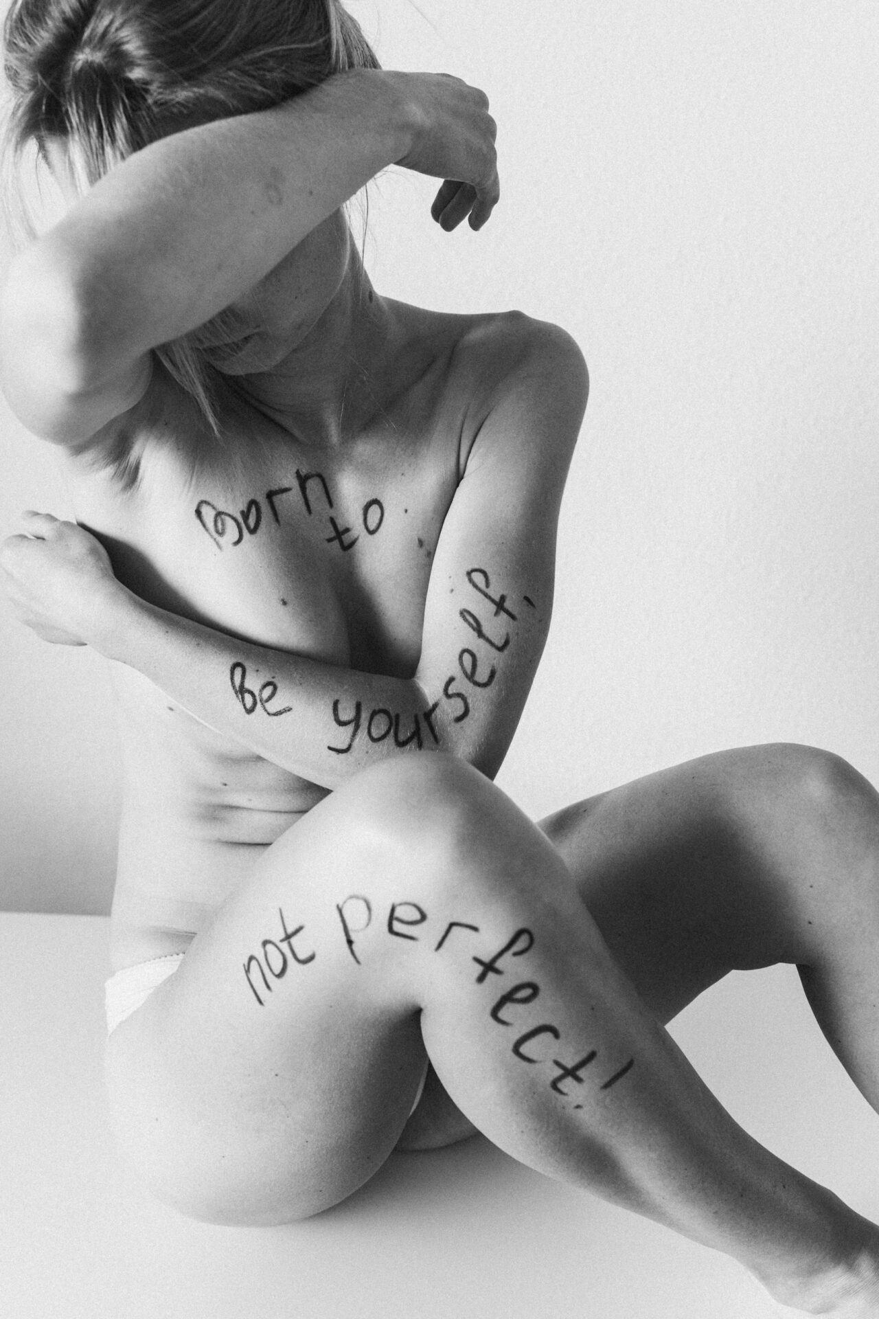 Black and white portrait of a woman embracing herself with inspiring slogans on her skin.