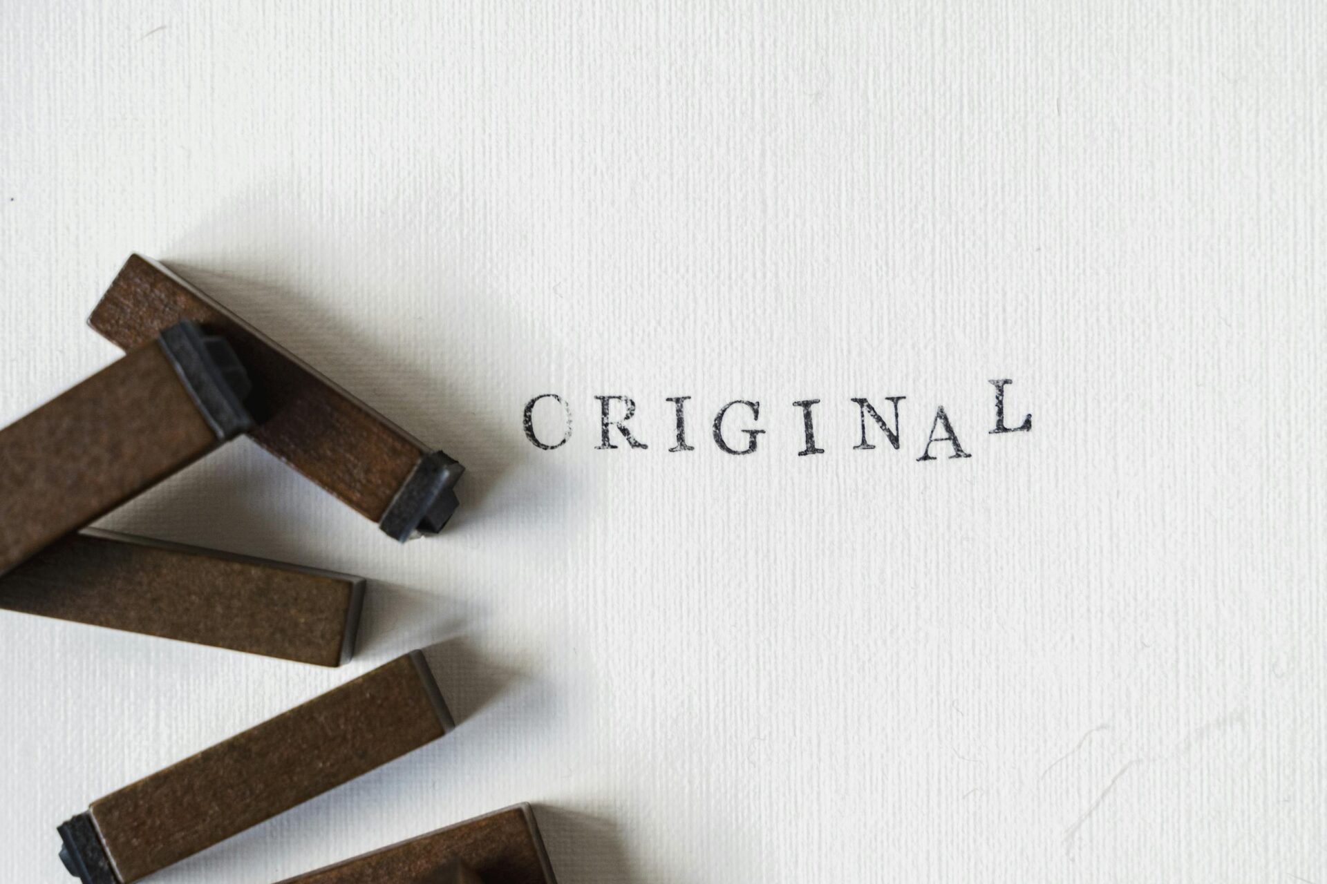 Wooden stamps spelling 'ORIGINAL' on textured paper, minimalistic design.